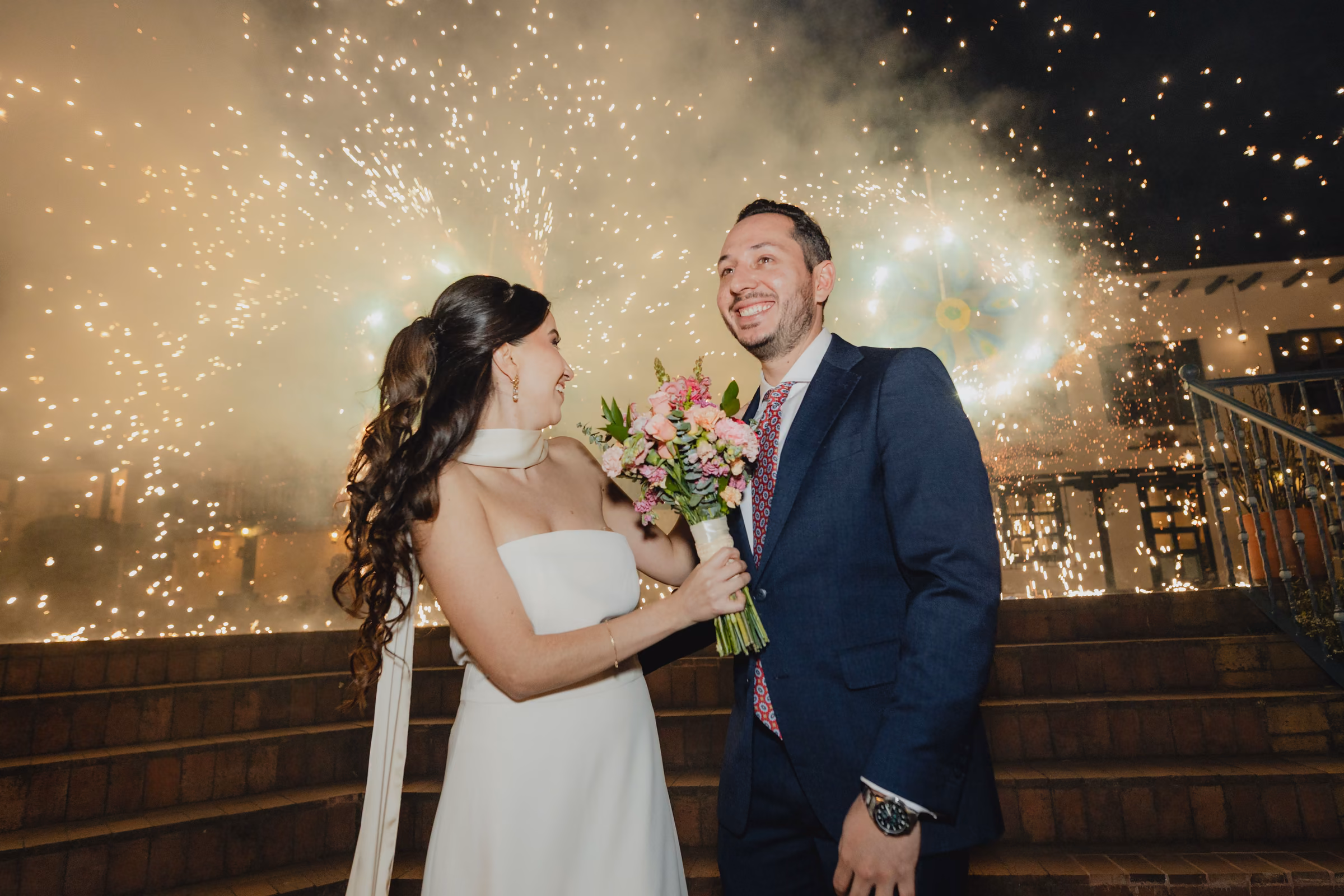 The couple framed by a curtain of cold sparks at night in the Estancia Rosario courtyard.
