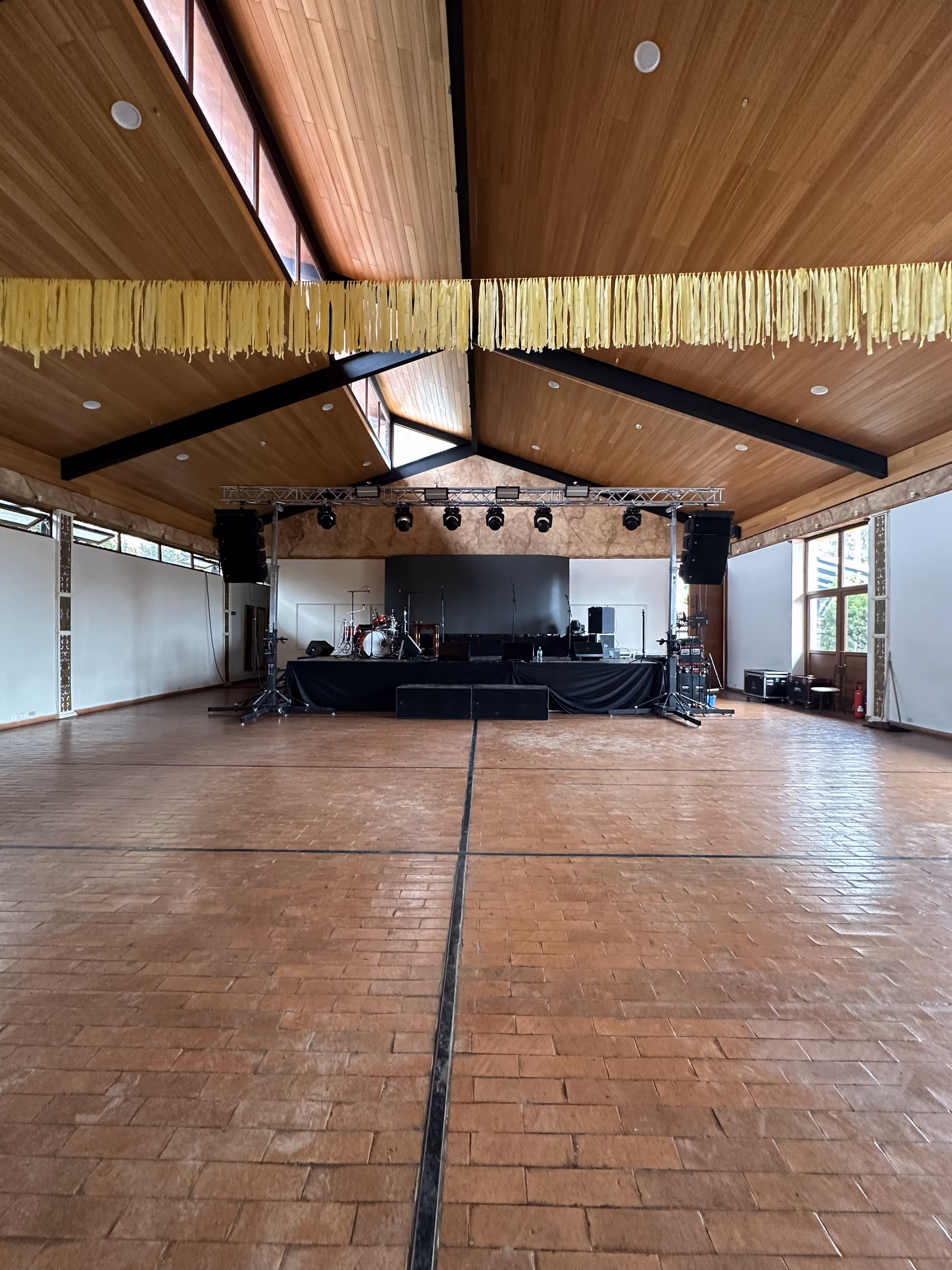 The empty hall with a stage, lighting truss and sound system rigged for a concert, under the gabled timber ceiling.