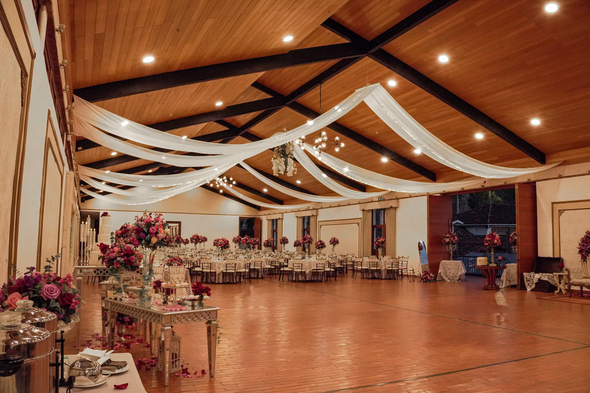 The Los Sauces hall set for an evening wedding, with white fabric draped from the timber ceiling and fuchsia floral centerpieces on the tables.