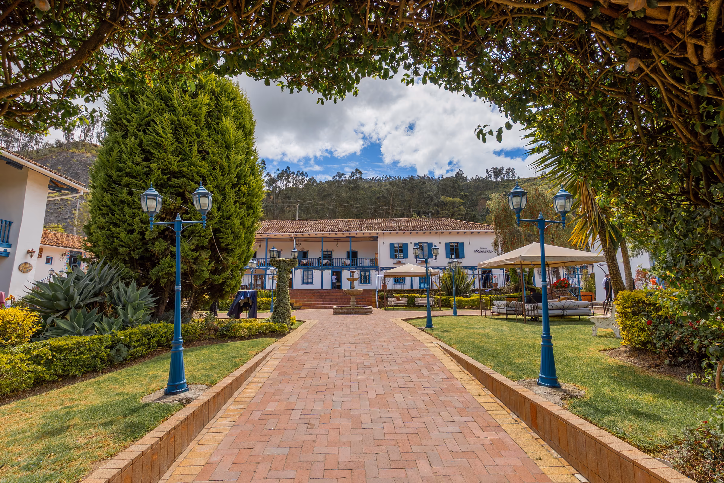 A brick path lined with blue lanterns leading to the main house, framed by overhanging branches.