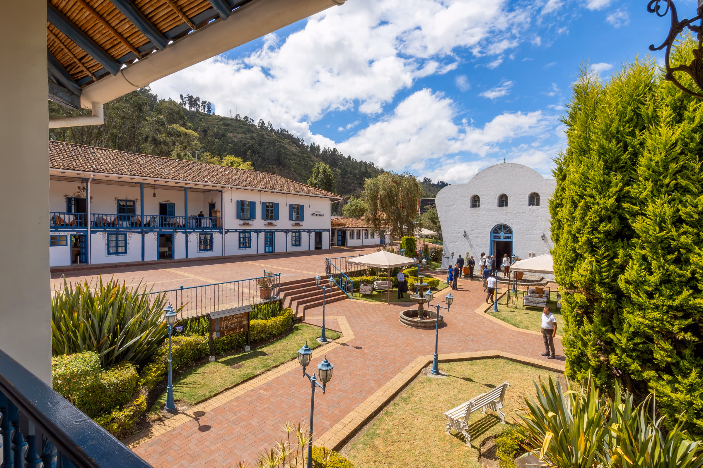 A balcony view over the brick courtyard, the blue-shuttered main house and the white chapel framed by gardens.